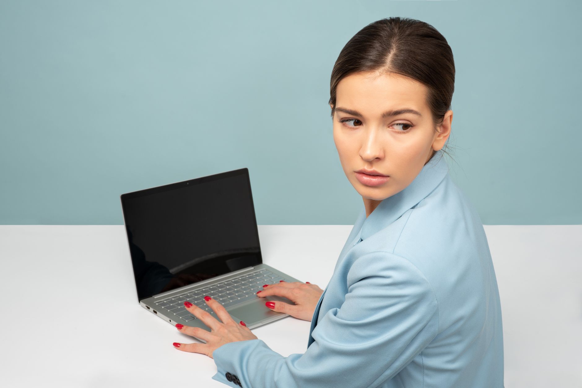 Businesswoman in blue suit using laptop, glancing over shoulder.