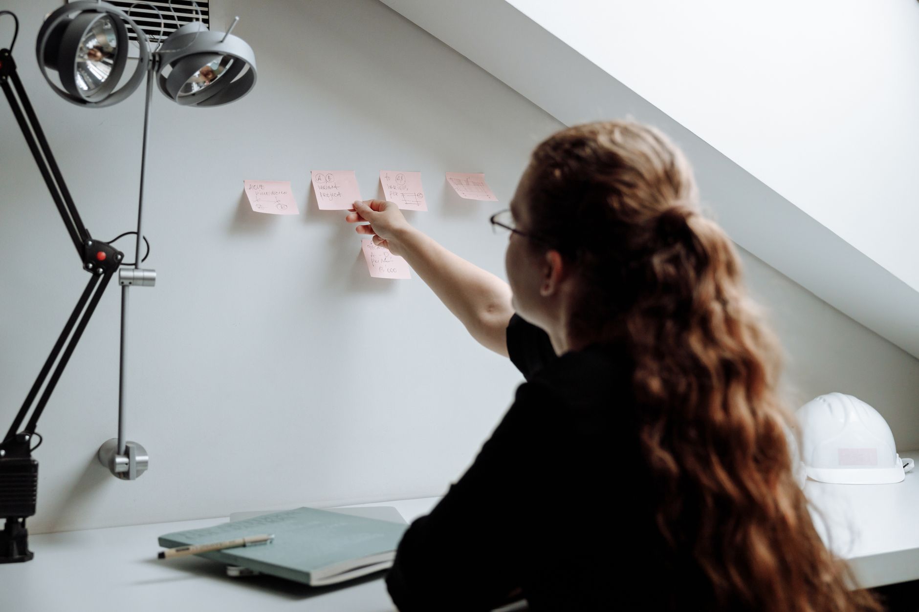 A woman organizes sticky notes on a wall in a sleek and modern office setting, promoting productivity and focus.