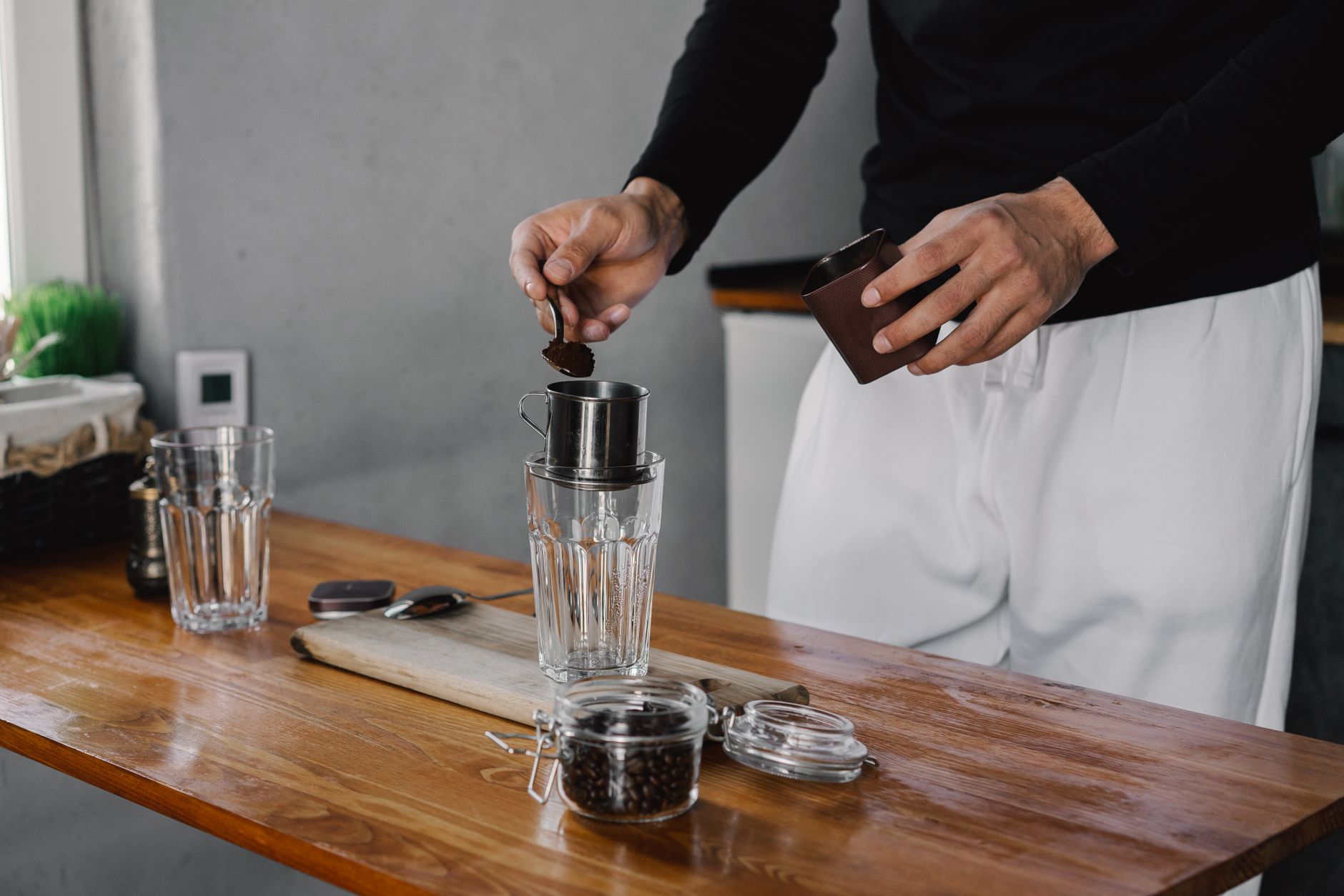 A person preparing coffee using a filter on a wooden table indoors.