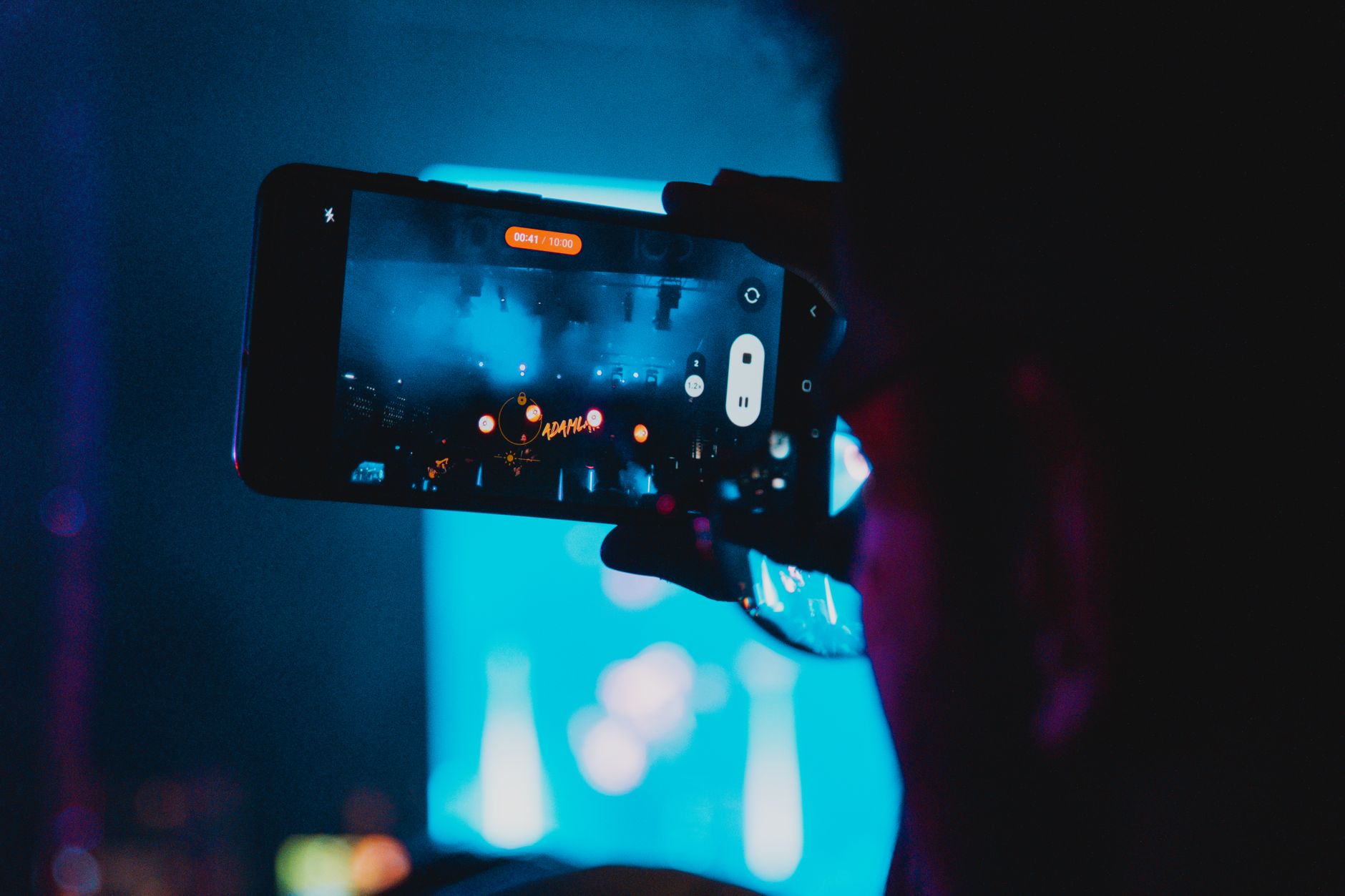 Close-up of a person filming a concert with a smartphone, capturing vibrant stage lights and atmosphere.