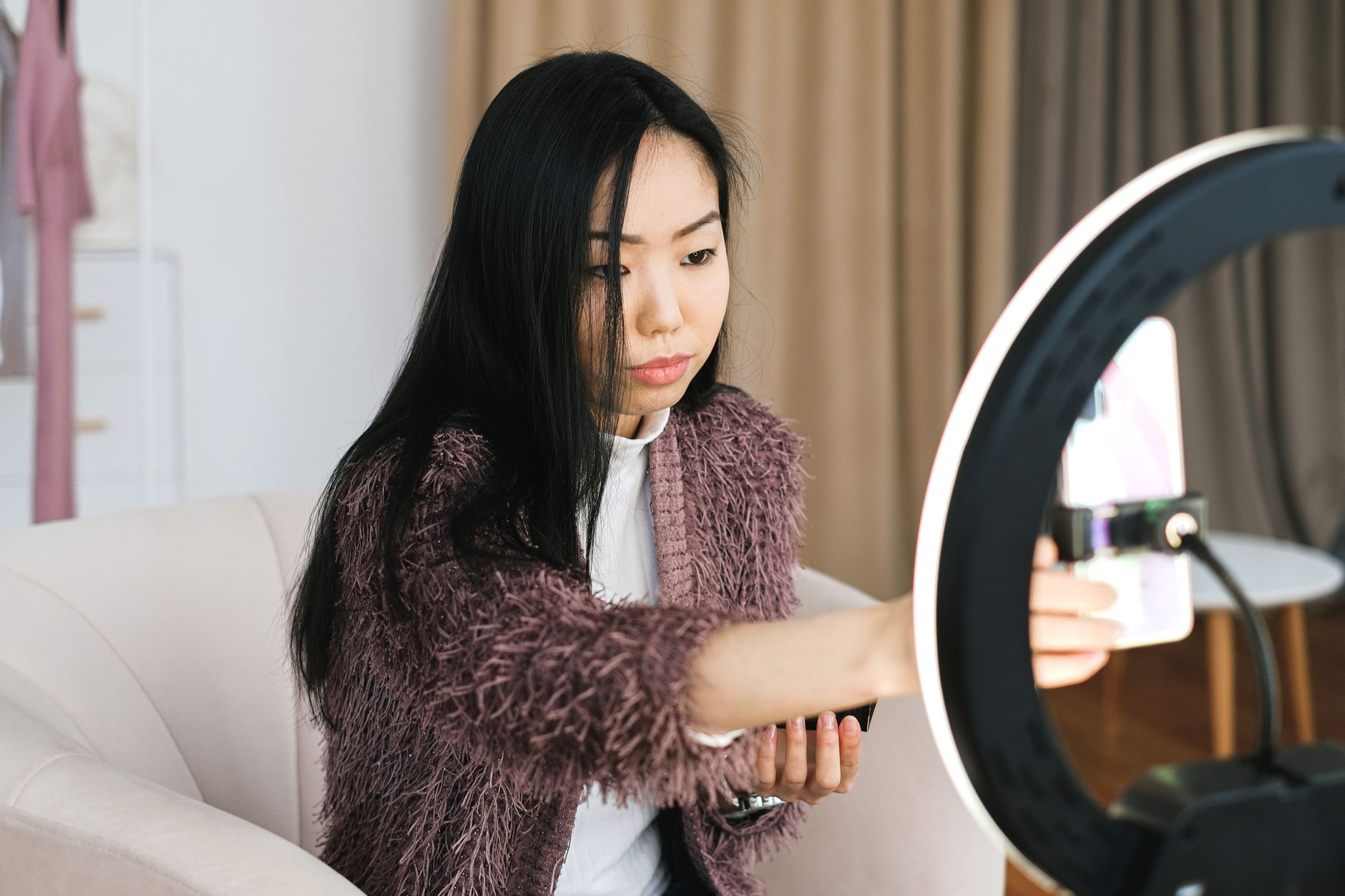 An Asian woman vlogs at home using a smartphone and ring light, perfect setup for influencers.