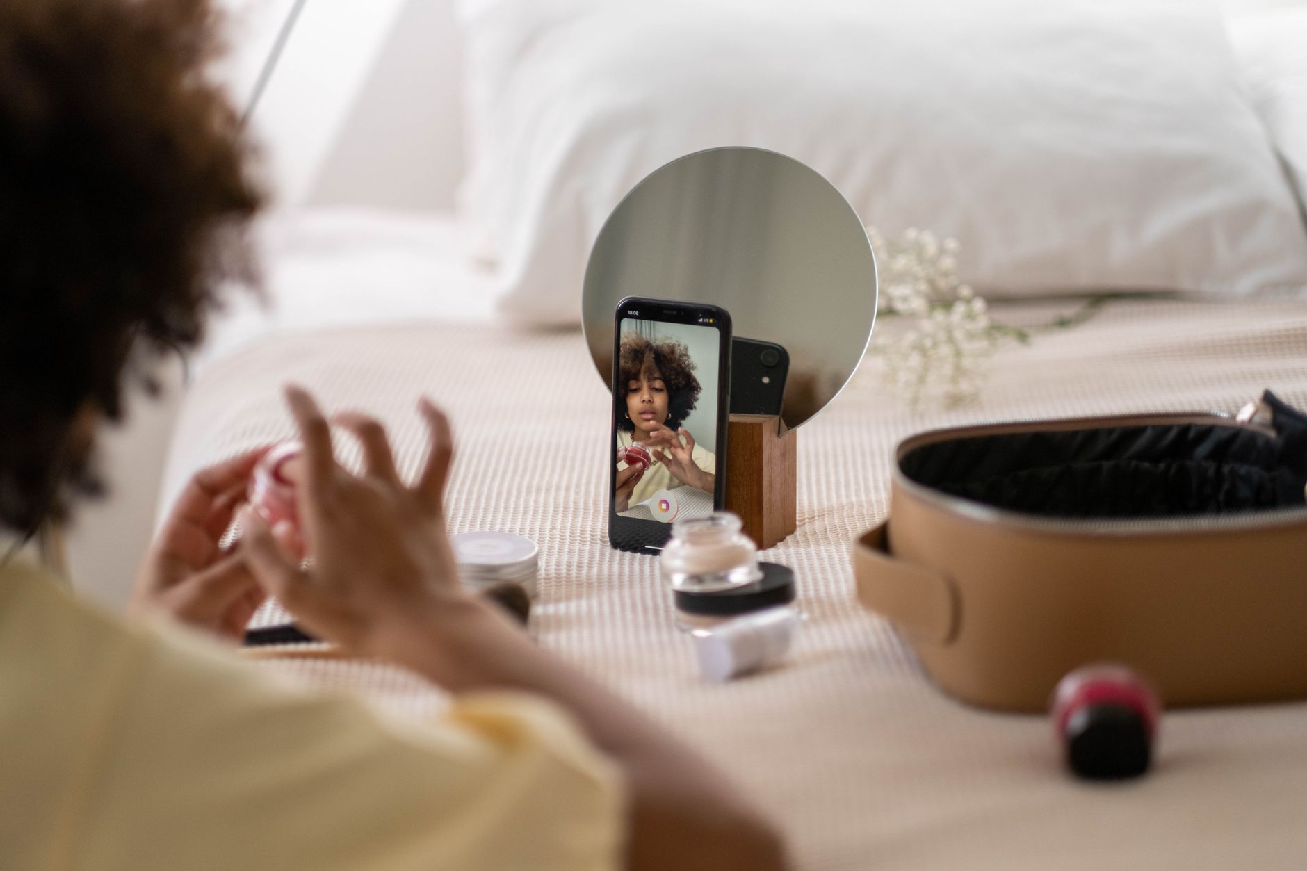 Woman recording a skincare vlog with cosmetics using a phone camera indoors.